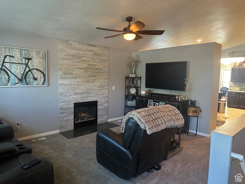 Carpeted living area featuring ceiling fan, a fireplace, baseboards, and a textured ceiling