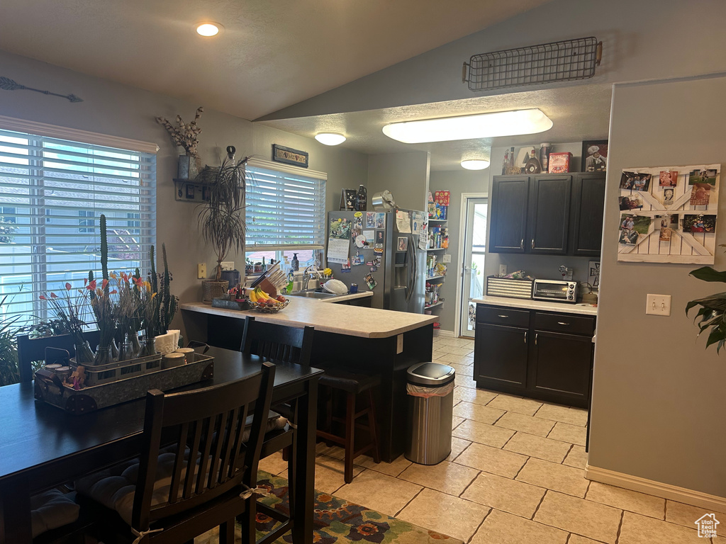 Kitchen with stainless steel refrigerator with ice dispenser, vaulted ceiling, light countertops, plenty of natural light, and a peninsula