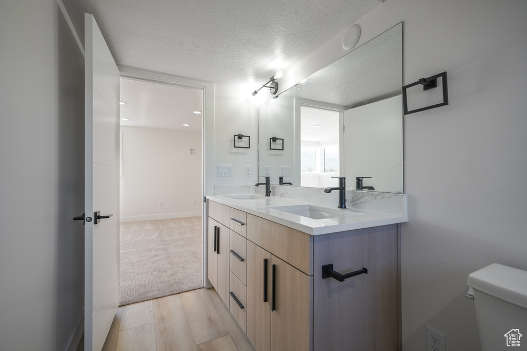 Full bath featuring double vanity, a textured ceiling, toilet, wood finished floors, and baseboards