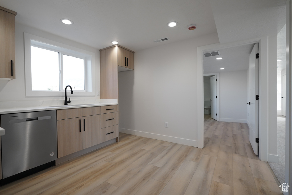 Kitchen with a sink, stainless steel dishwasher, light brown cabinets, light wood-style floors, and light countertops