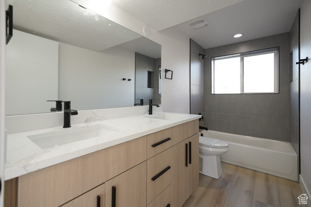 Bathroom featuring wood finished floors, toilet, double vanity,  shower combination, and a textured ceiling
