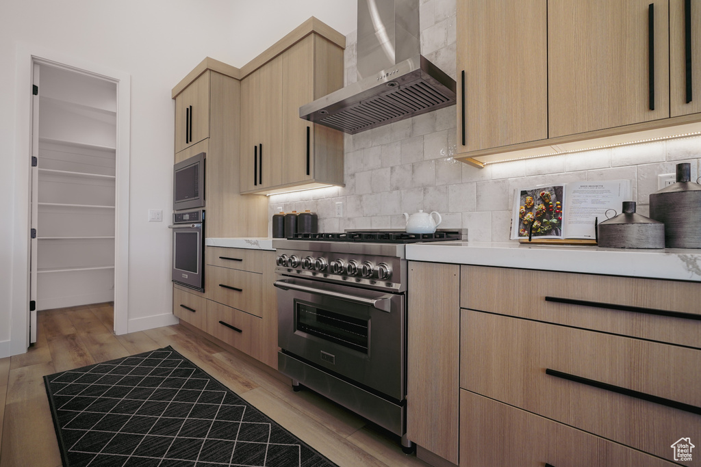 Kitchen featuring wall chimney exhaust hood, stainless steel appliances, light brown cabinets, and backsplash