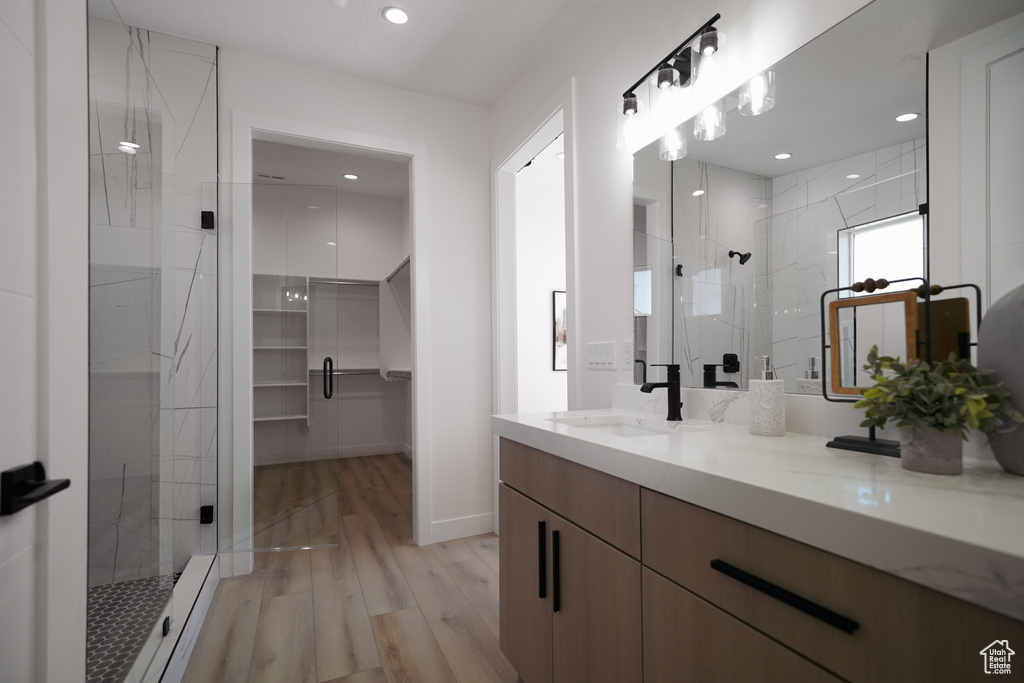 Full bath featuring a shower stall, double vanity, wood finished floors, a walk in closet, and recessed lighting