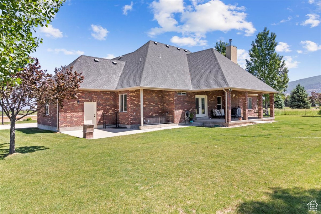 Back of property featuring brick siding, a yard, a chimney, and a patio