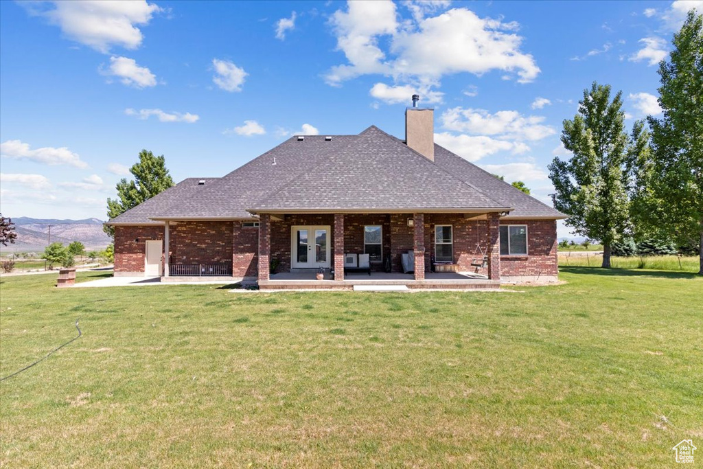 Back of property featuring a chimney, brick siding, a yard, french doors, and roof with shingles