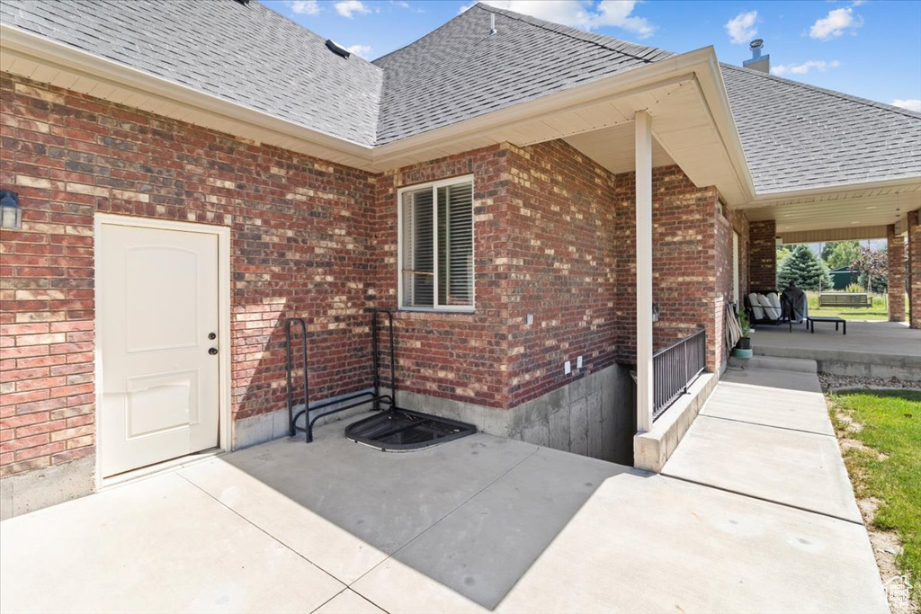 Property entrance with a shingled roof, brick siding, and covered porch