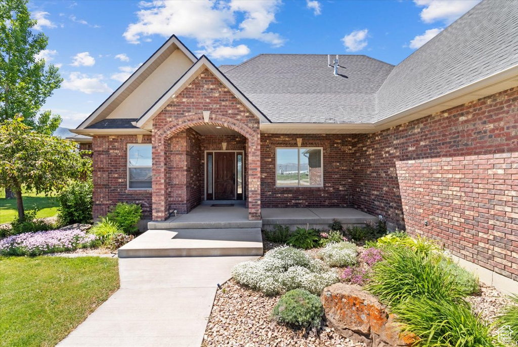 Property entrance with a porch, brick siding, and roof with shingles