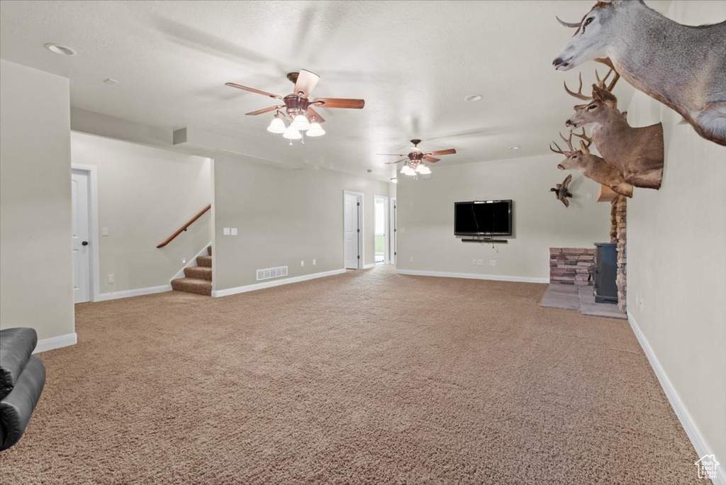 Unfurnished living room with carpet floors, stairs, ceiling fan, and a wood stove