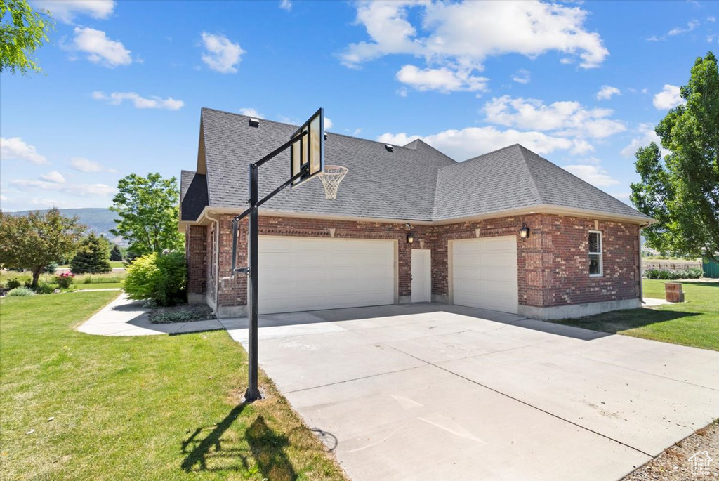 View of side of property with an attached garage, brick siding, a lawn, and roof with shingles
