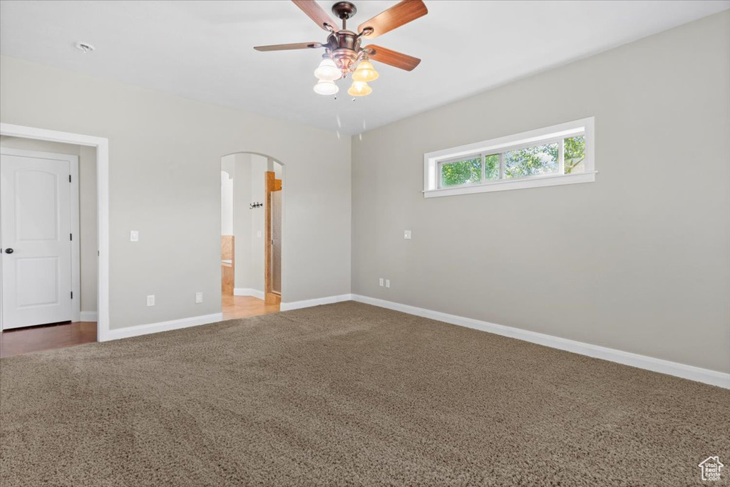 Unfurnished bedroom with carpet floors, arched walkways, baseboards, ensuite bathroom, and ceiling fan