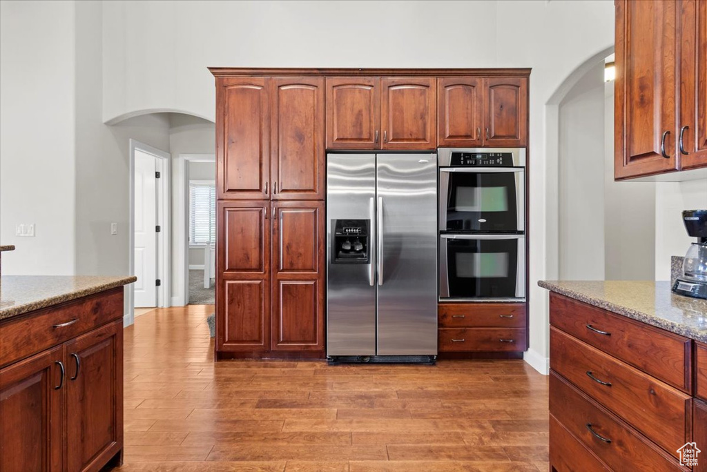 Kitchen featuring stainless steel appliances, arched walkways, light stone counters, and light wood finished floors