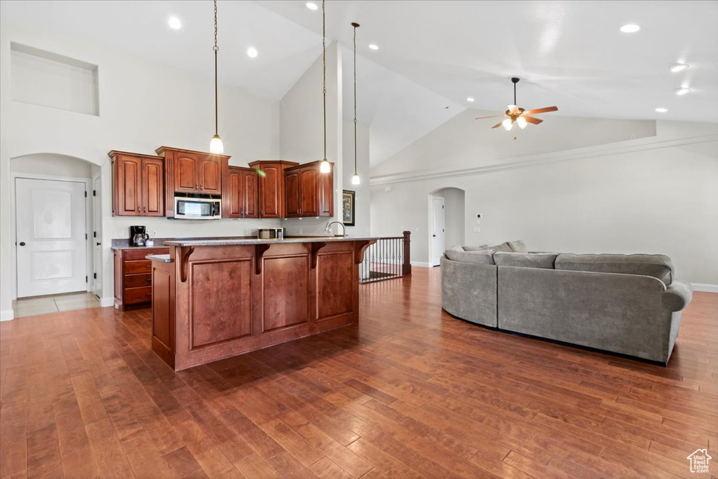 Kitchen featuring stainless steel microwave, arched walkways, a breakfast bar area, a ceiling fan, and high vaulted ceiling