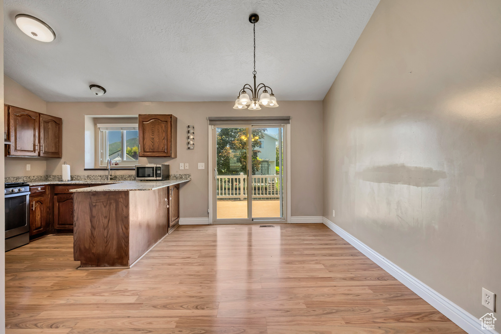 Kitchen with appliances with stainless steel finishes, light wood finished floors, a peninsula, hanging light fixtures, and a textured ceiling