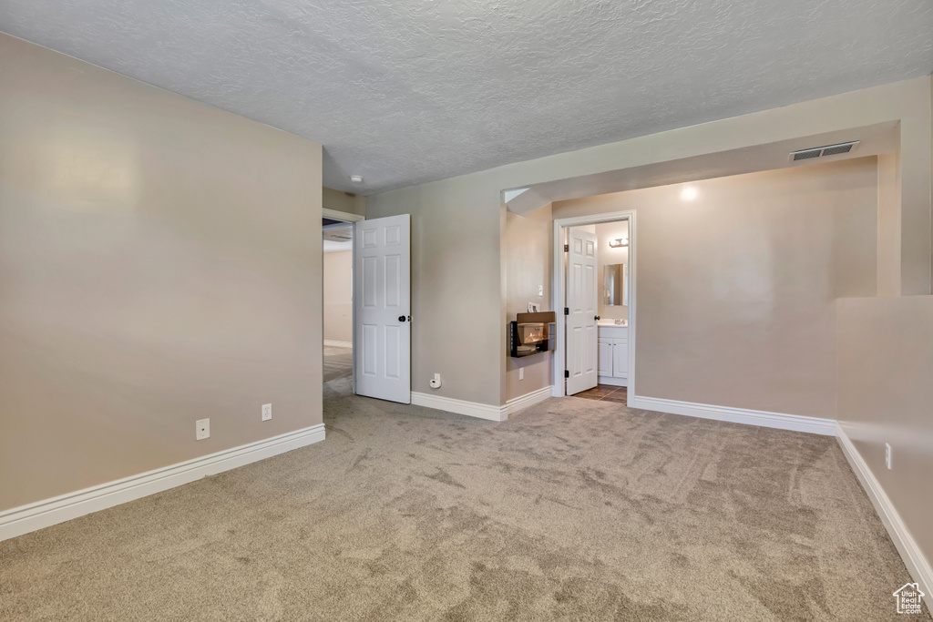 Unfurnished bedroom with carpet, baseboards, a textured ceiling, and connected bathroom