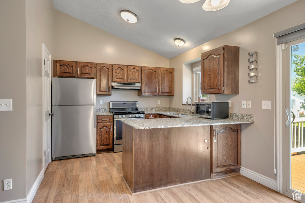 Kitchen featuring stainless steel appliances, under cabinet range hood, a peninsula, a sink, and light wood finished floors