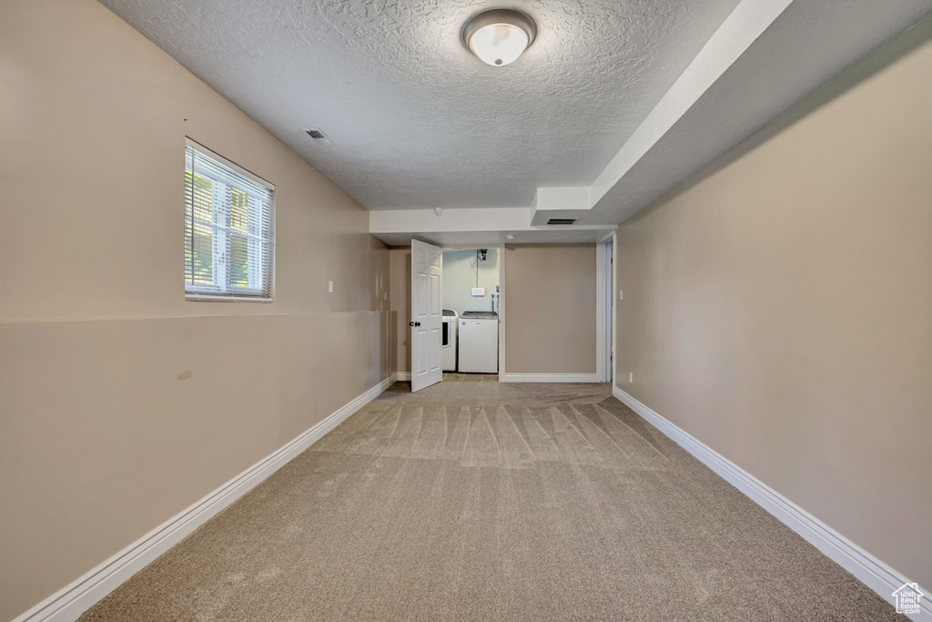 Empty room featuring a textured ceiling, independent washer and dryer, light carpet, and baseboards