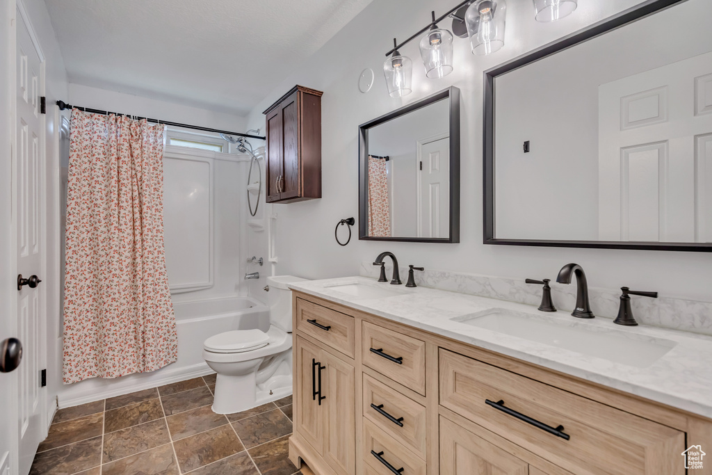 Full bathroom featuring double vanity, shower / bath combo with shower curtain, toilet, and stone finish flooring