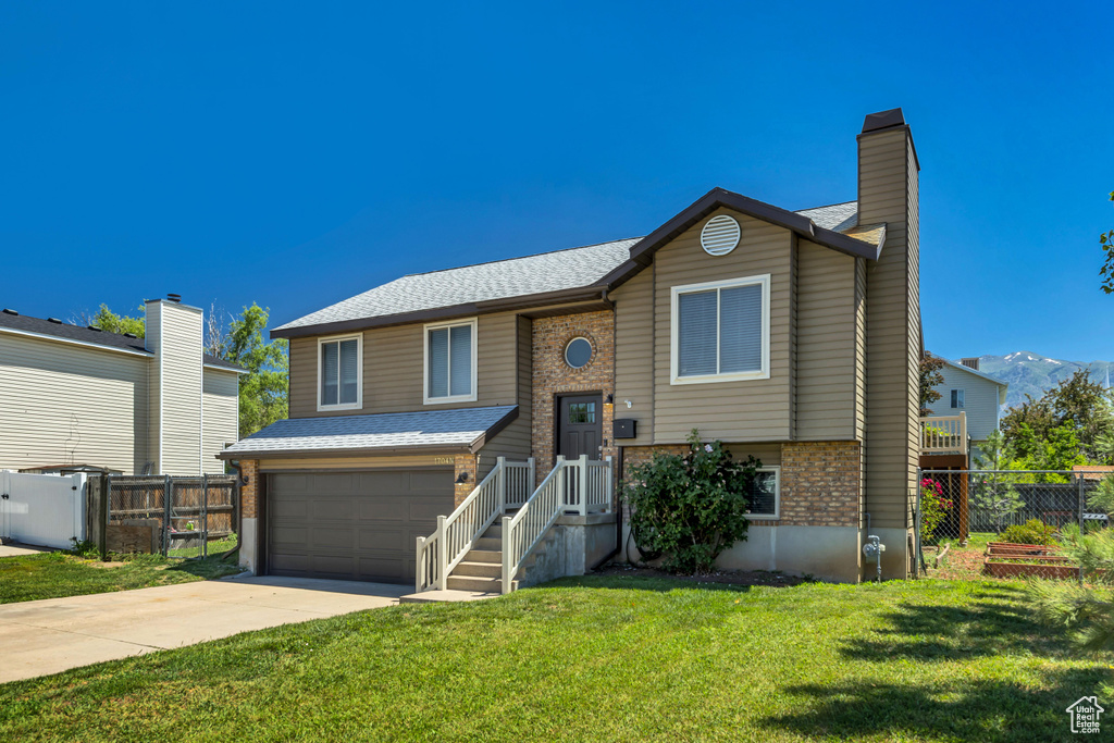 Split foyer home featuring brick siding, driveway, an attached garage, and a chimney