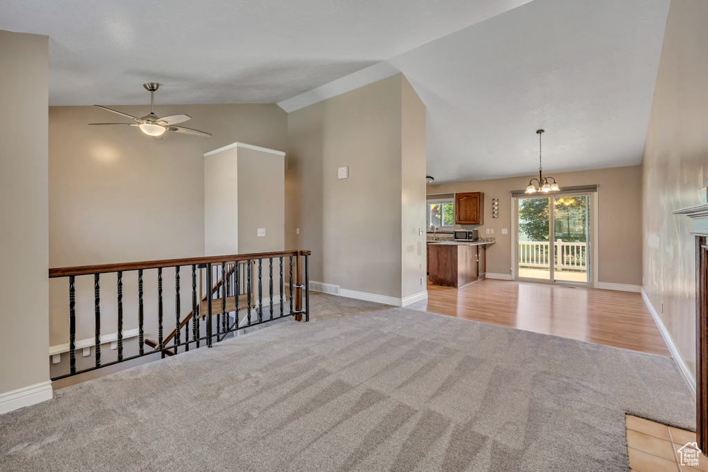 Unfurnished room with light colored carpet, lofted ceiling, a chandelier, ceiling fan, and baseboards