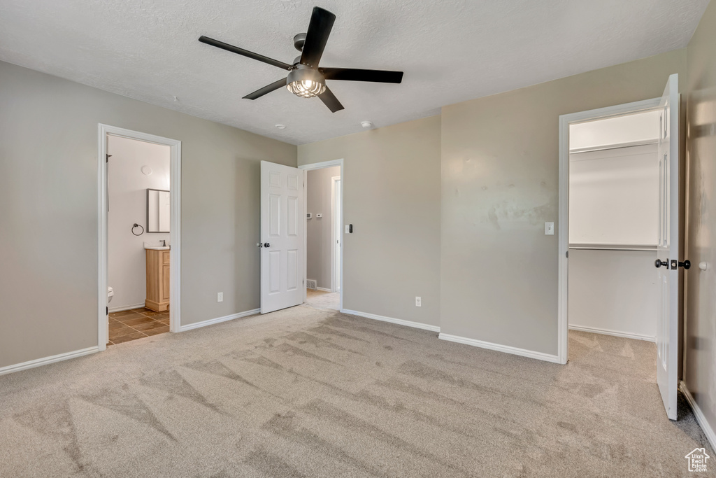 Unfurnished bedroom featuring carpet, a spacious closet, baseboards, connected bathroom, and a ceiling fan