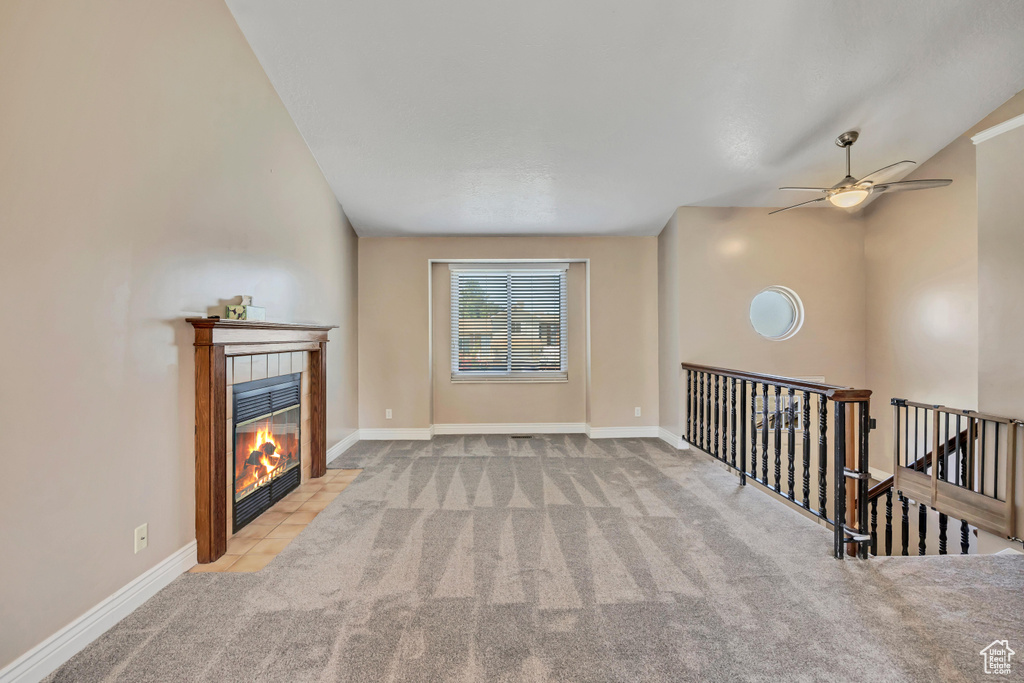Unfurnished living room featuring carpet flooring, a tile fireplace, ceiling fan, baseboards, and lofted ceiling