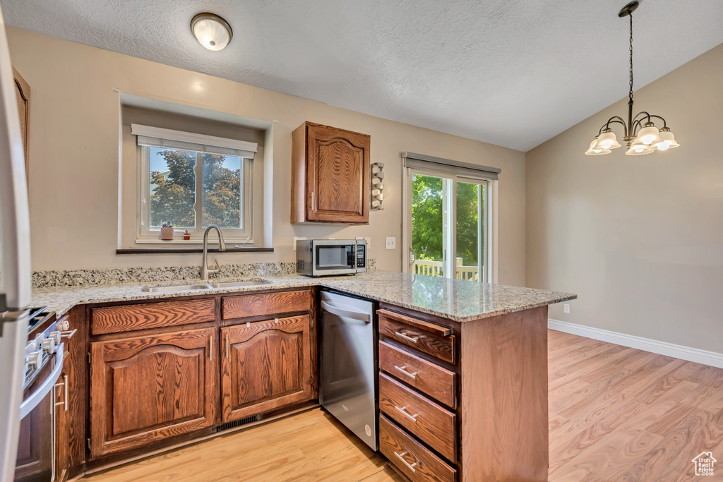 Kitchen with stainless steel appliances, a sink, a peninsula, light wood-type flooring, and a textured ceiling