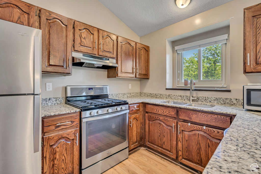Kitchen featuring appliances with stainless steel finishes, under cabinet range hood, a sink, lofted ceiling, and light wood finished floors