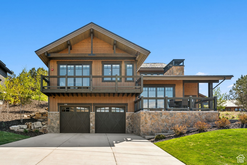 View of front of home with stone siding, driveway, a chimney, a front yard, and an attached garage