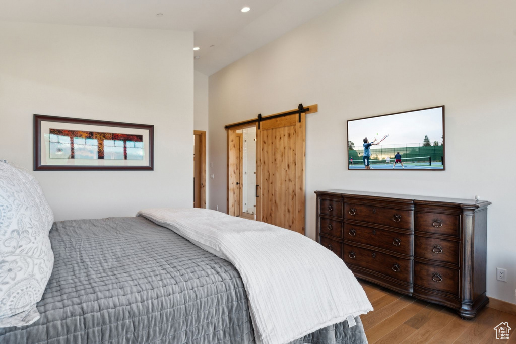 Bedroom with light wood-type flooring, a barn door, a high ceiling, and recessed lighting