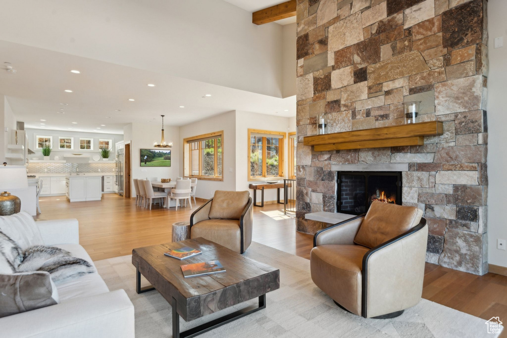 Living room with light wood finished floors, recessed lighting, a stone fireplace, a chandelier, and beamed ceiling