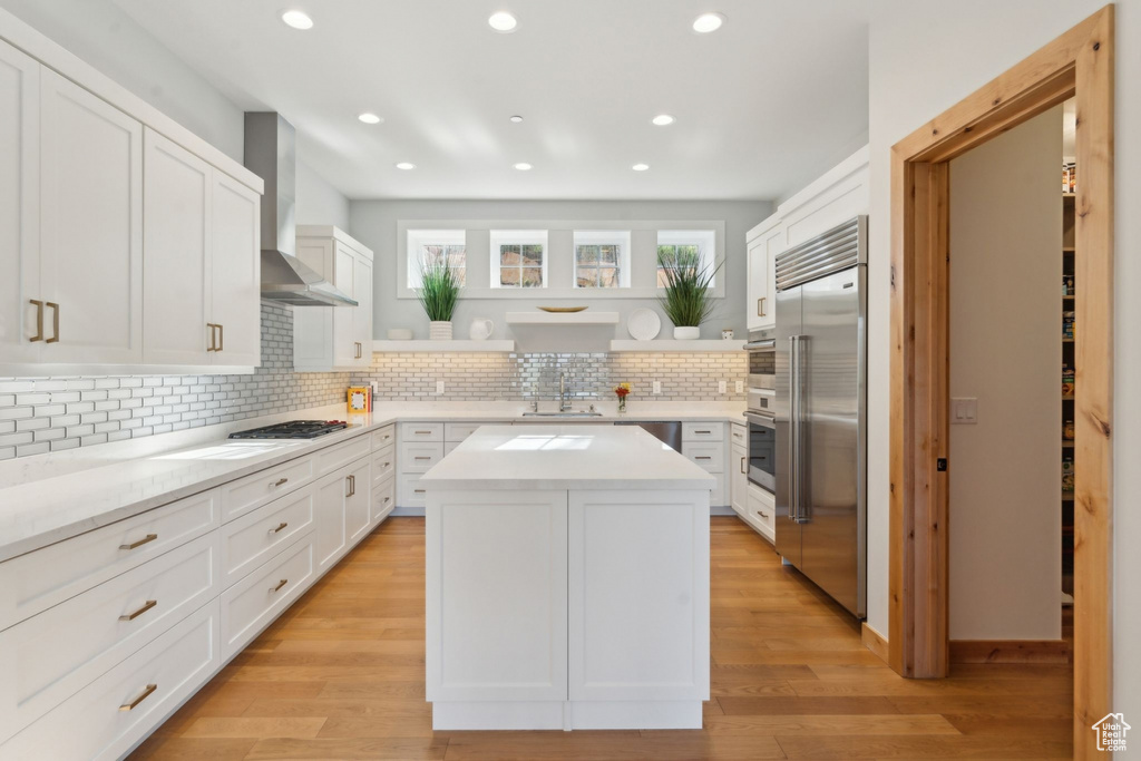 Kitchen with appliances with stainless steel finishes, wall chimney range hood, a sink, backsplash, and recessed lighting