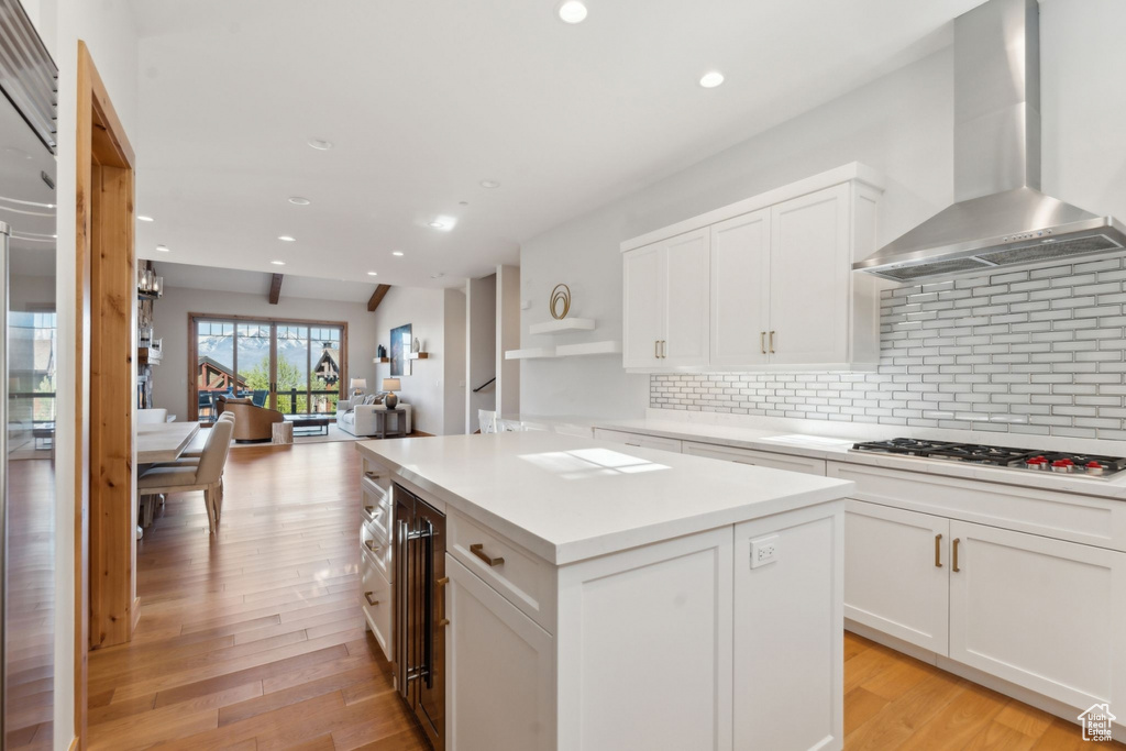Kitchen featuring wall chimney exhaust hood, stainless steel gas stovetop, a center island, decorative backsplash, and white cabinetry