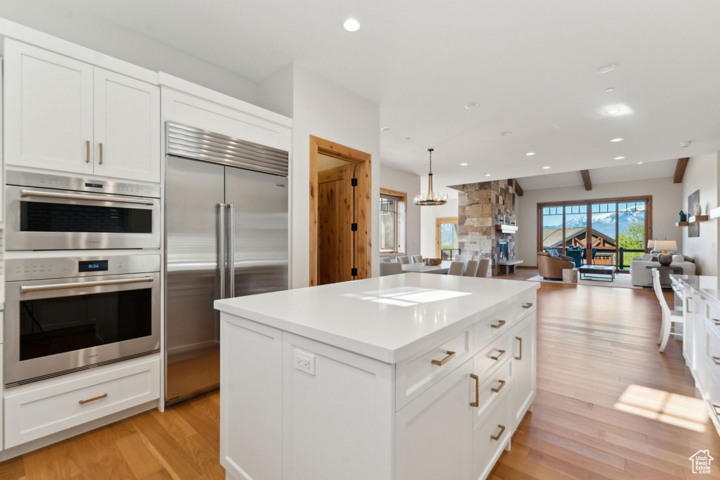 Kitchen featuring appliances with stainless steel finishes, open floor plan, light wood-type flooring, white cabinets, and a kitchen island