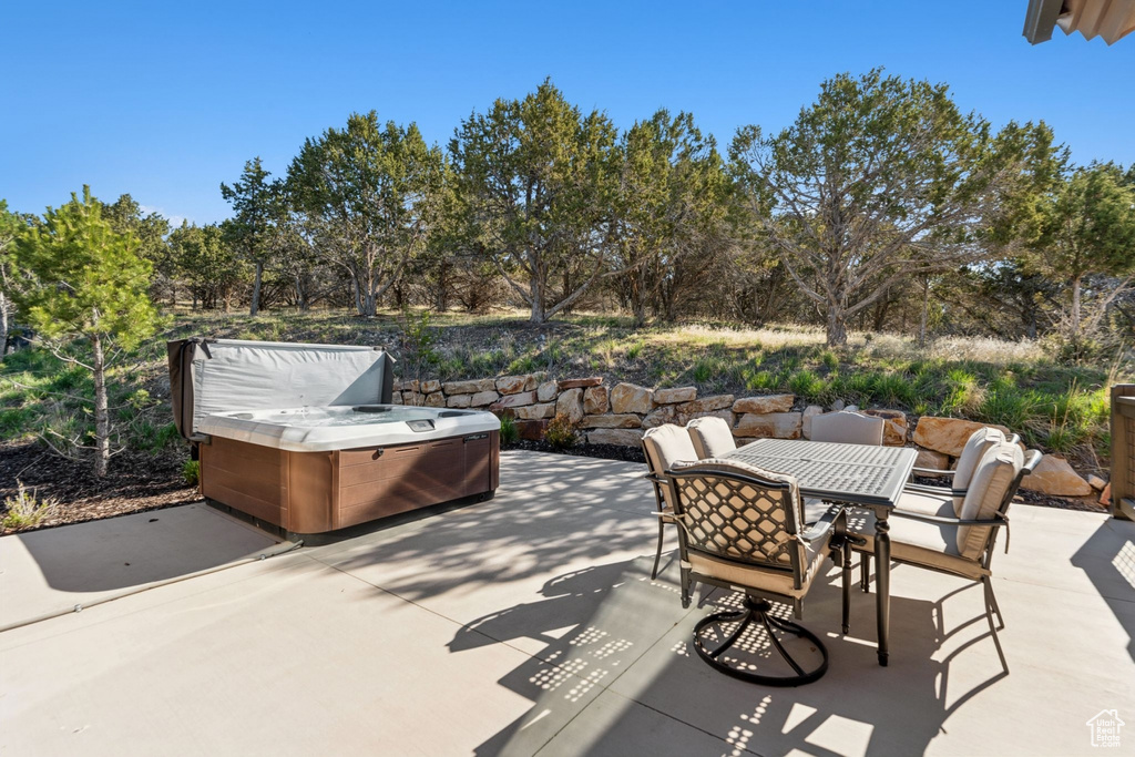 View of patio / terrace with a hot tub, outdoor dining space, and view of scattered trees