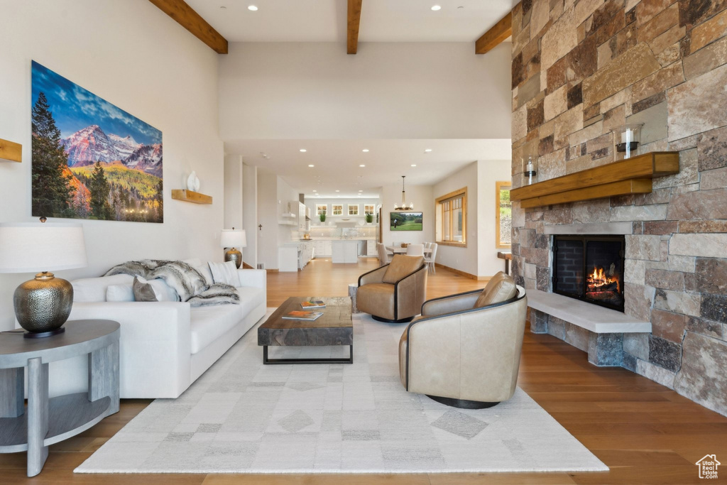Living room featuring a high ceiling, beamed ceiling, a fireplace, wood finished floors, and recessed lighting