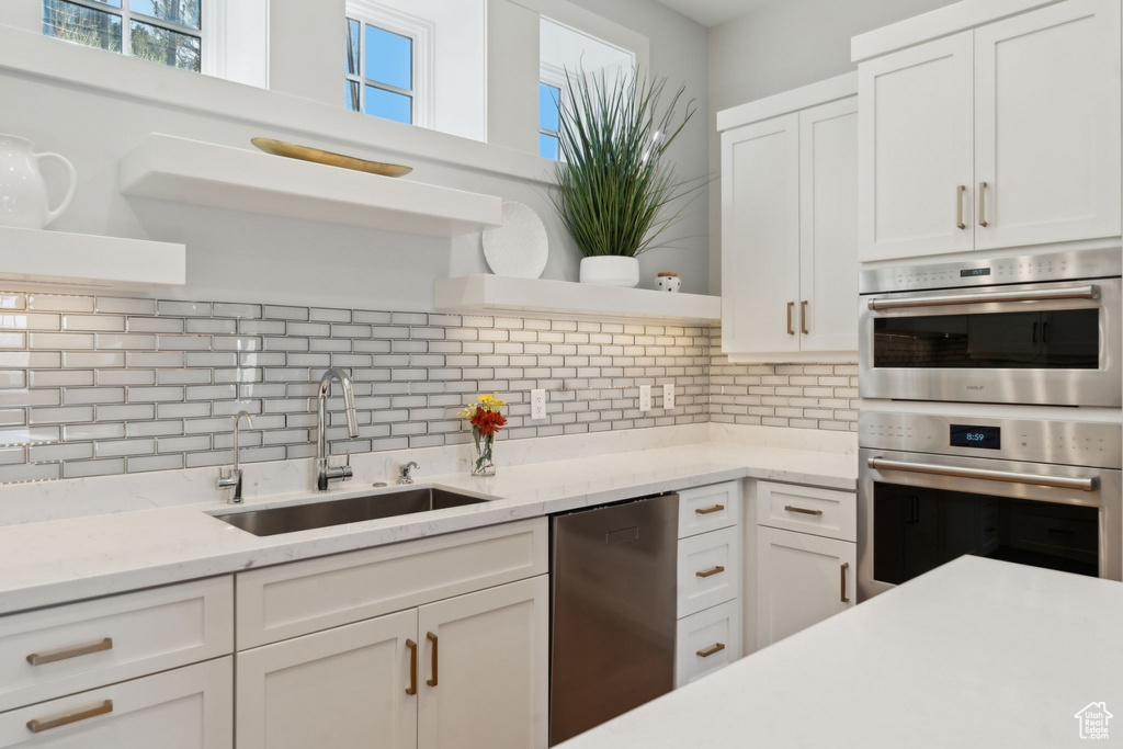 Kitchen with open shelves, a sink, stainless steel appliances, white cabinets, and decorative backsplash