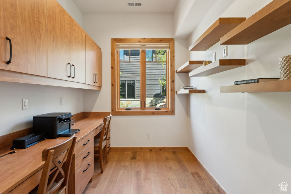 Office space with light wood finished floors, built in desk, and baseboards