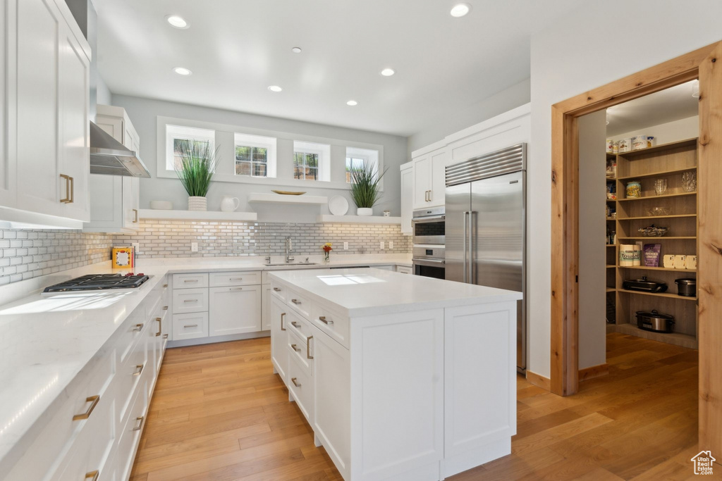 Kitchen featuring appliances with stainless steel finishes, open shelves, a sink, decorative backsplash, and light wood-type flooring