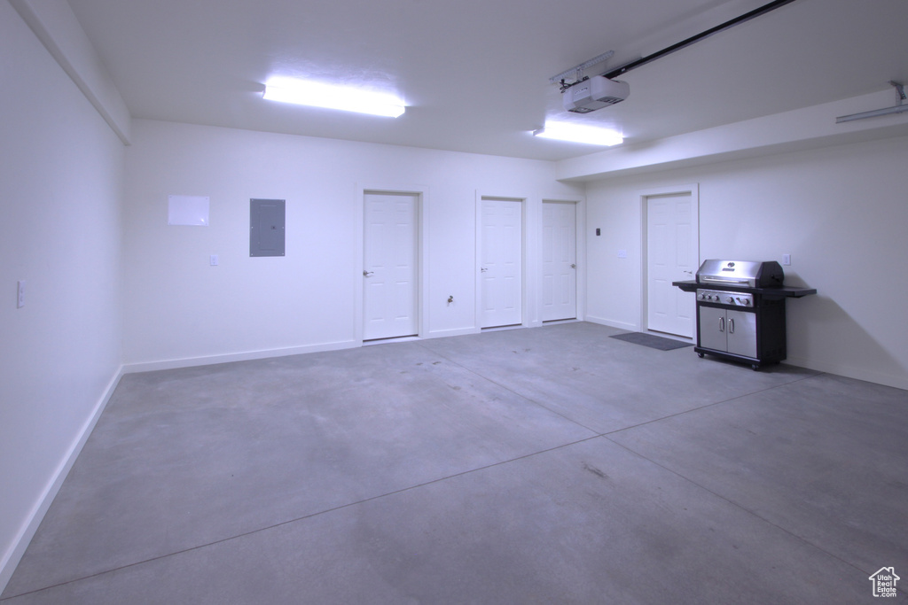 Garage featuring electric panel, baseboards, and a garage door opener