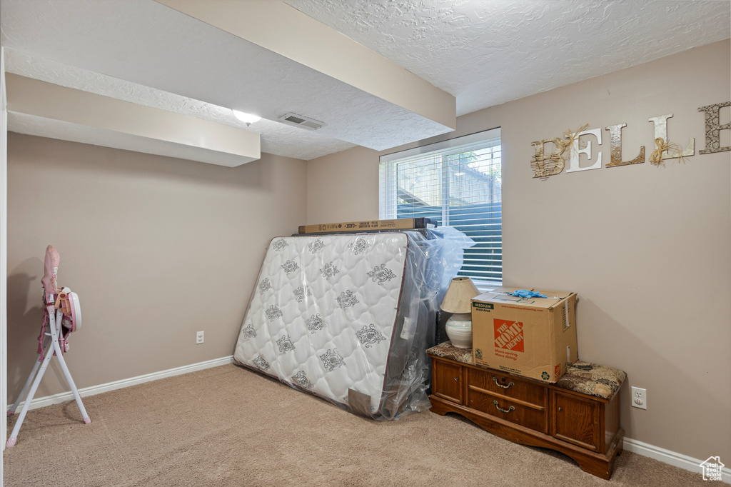Bedroom with a textured ceiling, light carpet, and baseboards