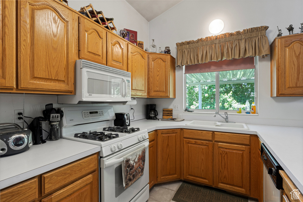 Kitchen with white appliances, a sink, vaulted ceiling, light countertops, and brown cabinets