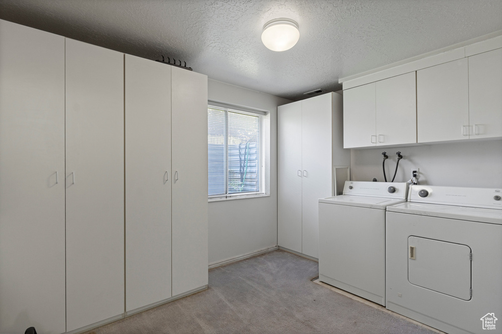 Washroom featuring washing machine and dryer, cabinet space, light carpet, and a textured ceiling