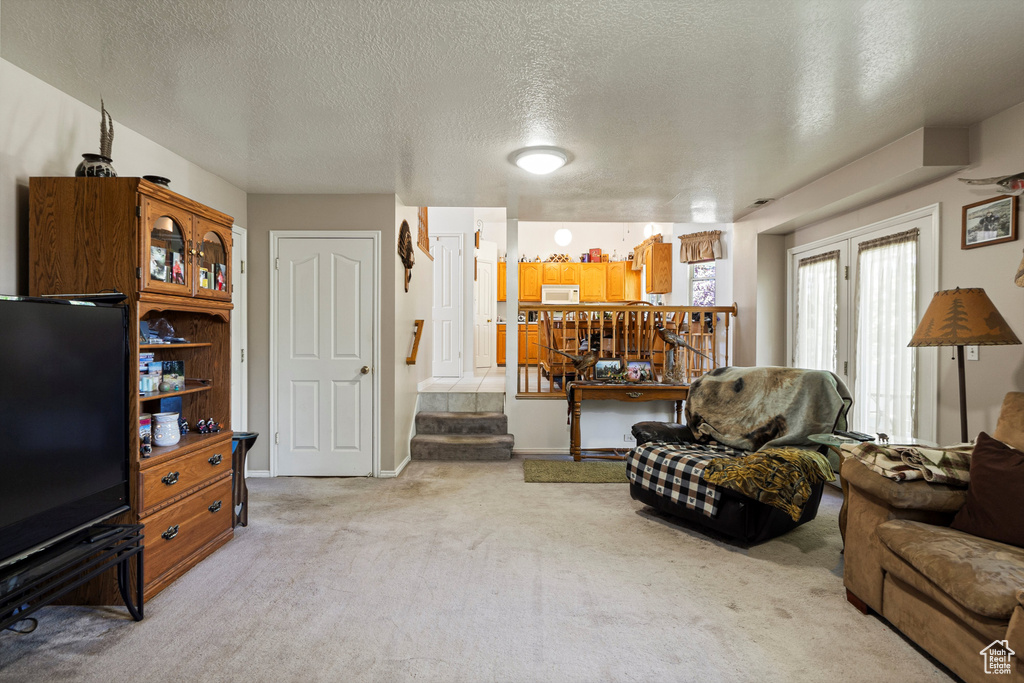 Living area featuring a textured ceiling, light colored carpet, and stairs