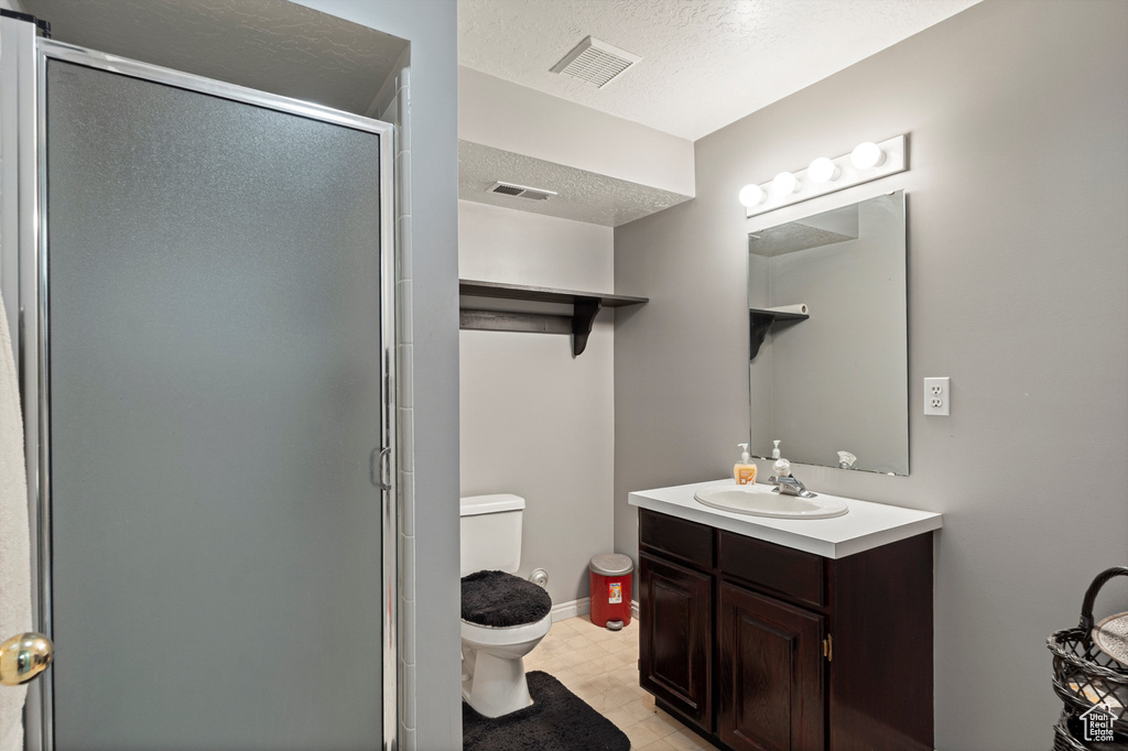 Full bath featuring toilet, vanity, a stall shower, a textured ceiling, and tile patterned floors