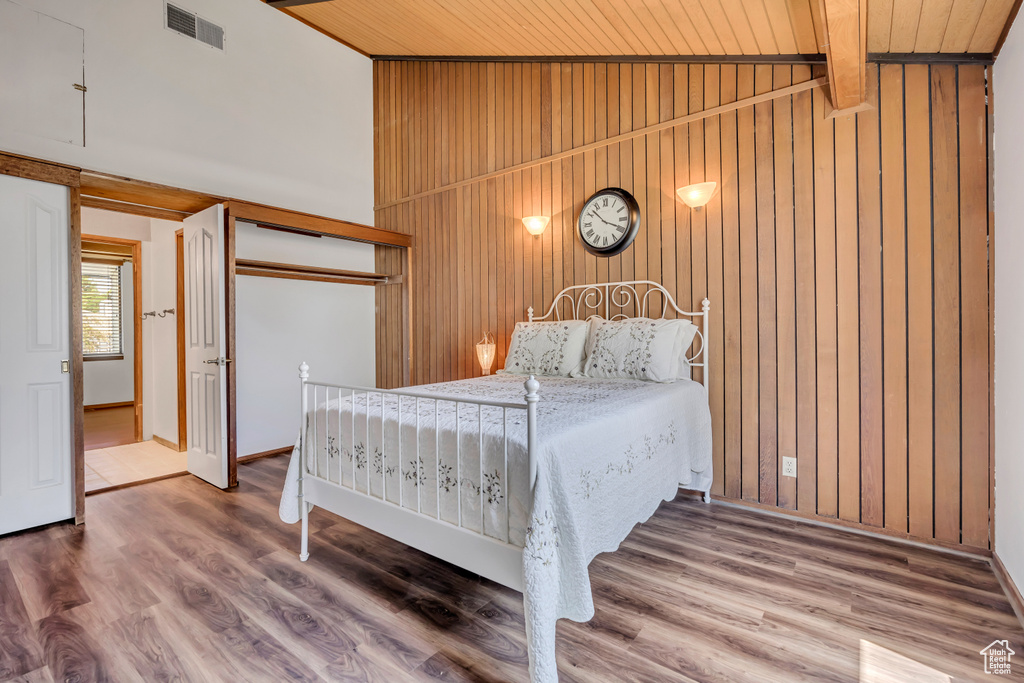 Bedroom with wood walls, wooden ceiling, wood finished floors, a closet, and high vaulted ceiling