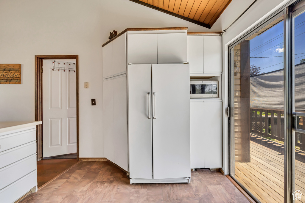 Kitchen featuring white fridge, stainless steel microwave, vaulted ceiling, white cabinets, and wooden ceiling