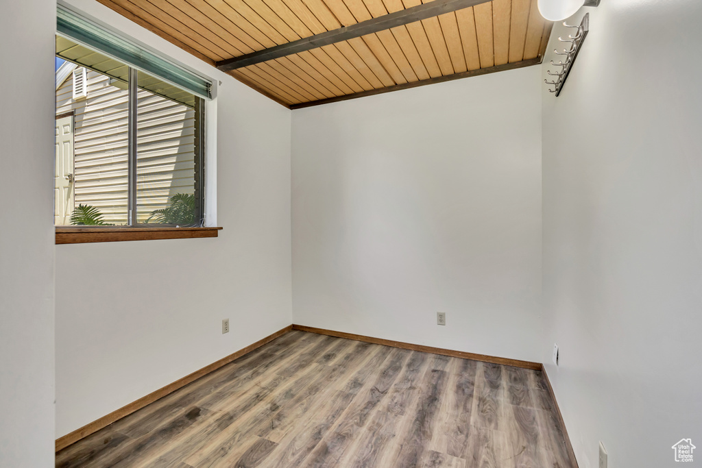 Unfurnished room with wooden ceiling with exposed beams, wood finished floors, and baseboards