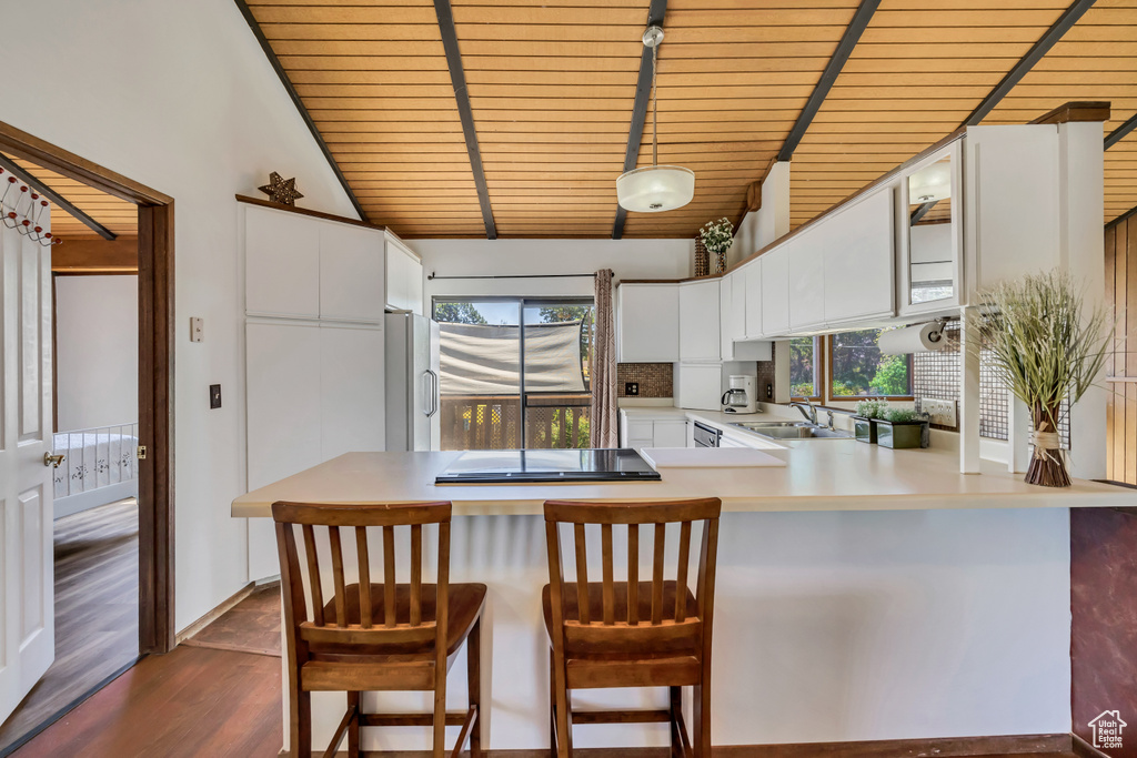 Kitchen featuring a peninsula, freestanding refrigerator, black electric cooktop, dark wood finished floors, and white cabinets