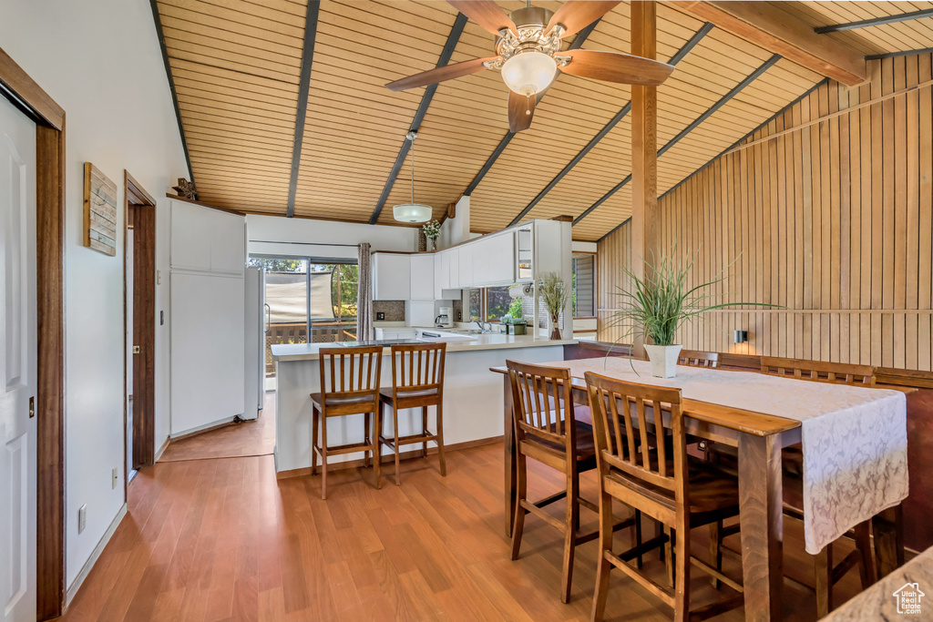 Dining room with light wood finished floors, ceiling fan, wooden ceiling with exposed beams, and high vaulted ceiling