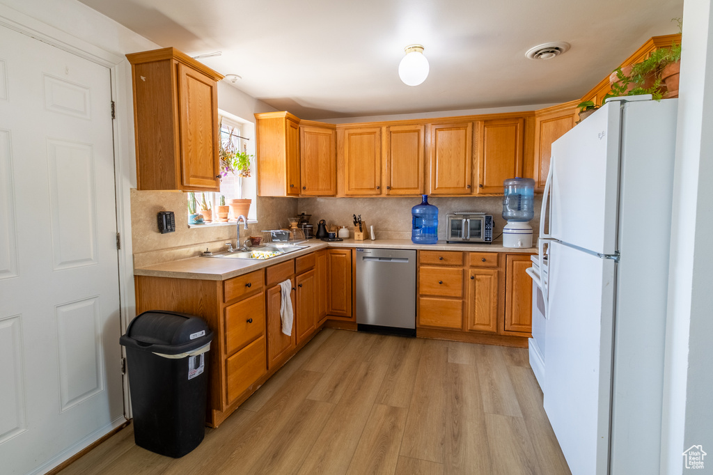 Kitchen with stainless steel dishwasher, freestanding refrigerator, a sink, light countertops, and light wood finished floors